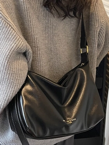 Sac bandoulière en cuir noir élégant avec boucles dorées porté par un mannequin