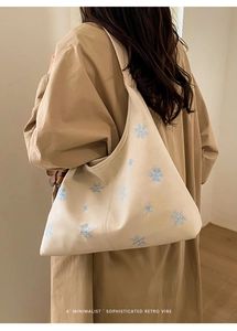 Detail of beige tote bag showing intricate blue snowflake embroidery and soft leather texture