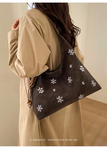 Close-up of retro brown shoulder bag with snowflake embroidery and floral pendant detail