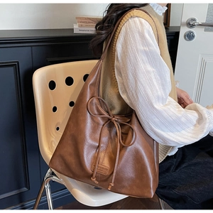 Detailed view of brown faux leather tote bag with bow drawstring and logo patch