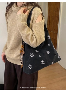 Detail of black tote bag with white snowflake embroidery and wooden bead tassel charm