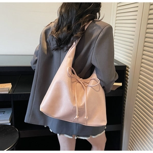 Pink faux leather tote bag detail with large bow accent worn over a grey blazer