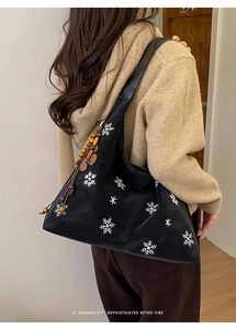 Detail of black tote bag with snowflake embroidery and wooden bead tassel ornament