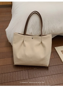 Detail of minimalist cream tote bag with brown leather handles and magnetic snap closure
