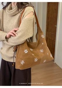 Detail of brown suede tote bag with white snowflake embroidery and beaded charm