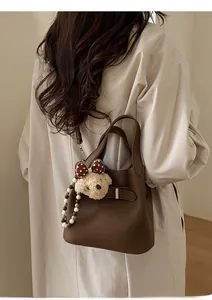 Detail of dark brown leather bucket bag with plush bear charm and beaded strap