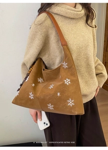 Detail of brown faux suede tote bag with snowflake embroidery and wooden bead charm accessory
