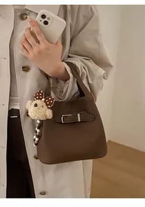 Detail of a brown lychee pattern leather bucket bag featuring a cute teddy bear charm