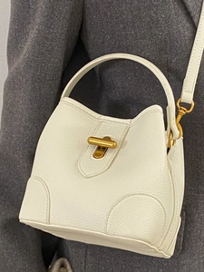 White pebbled leather bucket bag with gold metal clasp worn on a model against dark clothing