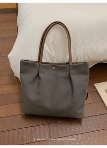 Detail of grey canvas tote bag with brown leather straps and minimalist logo on a white bed