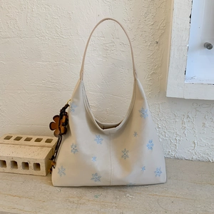Detail of off-white shoulder bag with blue snowflake embroidery and wooden bead charm