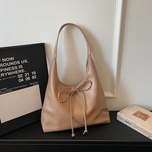 Detail view of khaki hobo bag with ribbon bow and embossed logo on minimalist background