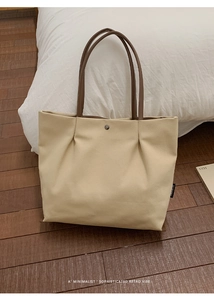 Close-up of beige canvas tote with pleated design and brown straps on wooden floor
