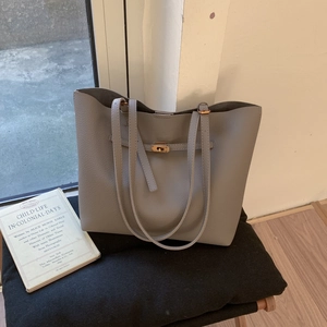 Detail of grey lychee texture leather tote bag with gold metal twist lock on a black stool
