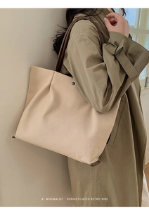 Minimalist beige canvas tote bag with brown strap shown as a lifestyle shoulder carry