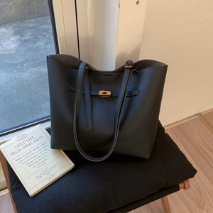 Classic black leather tote bag with gold metal lock buckle in a lifestyle setting