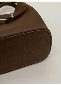 Detailed close-up showing the reinforced base and lychee grain texture of the brown leather bag