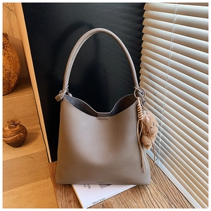 Détail du sac hobo en cuir gris avec breloque d'ours sur un bureau en bois ensoleillé