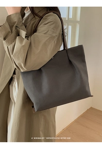 Minimalist large charcoal canvas tote bag with brown leather straps worn by a model