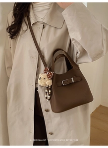Detail of dark brown leather bucket bag with silver metal clasp and plush bear charm