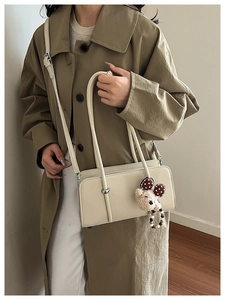Detail of cream baguette bag featuring textured leather and cute plush bear charm accessory
