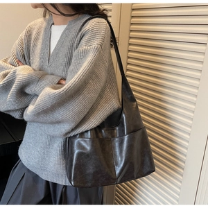 Detail of cross-stitched seams on a dark brown suede tote bag worn by a model