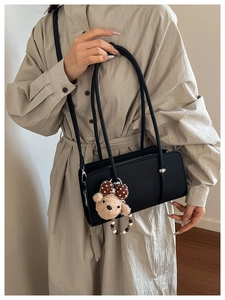 Chic black litchi leather baguette bag with plush bear charm worn by a model