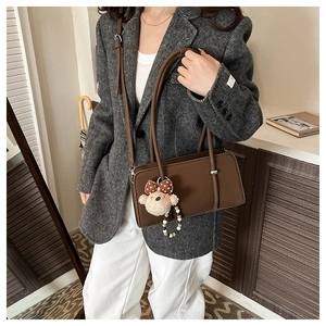 Detail view of deep brown faux leather baguette bag with textured finish and bear charm