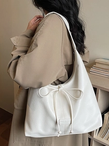Minimalist beige leather shoulder bag with bow detail worn by a model in fall style