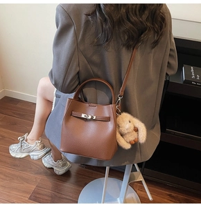 Sac seau en cuir marron avec fermoir argenté et breloque lapin porté par un mannequin
