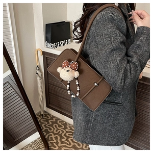 Detail of dark brown leather underarm bag with cute plush bear charm on grey wool coat