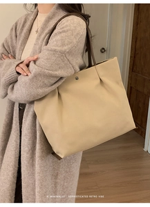 Detail of minimalist beige tote bag with brown leather handles and metal clasp shown on shoulder