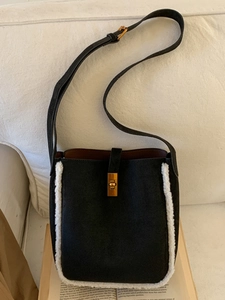 Modische schwarze Beuteltasche mit weißem Pelzbesatz und goldenem Drehverschluss am Buch
