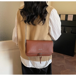 Detail of caramel brown pebble leather crossbody bag with chain strap and tassels