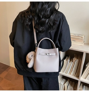 Détail du sac seau en cuir gris avec fermoir rotatif et pompon en peluche doux