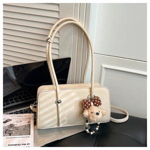 Detailed close-up of cream rectangular handbag with pebble leather and cute teddy bear charm