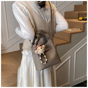Sac seau en cuir taupe avec pendentif ours en peluche sur un escalier d'intérieur