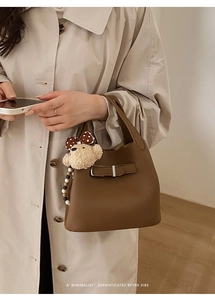 Detail of a brown lychee pattern leather handbag featuring a cute plush bear accessory