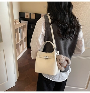 Détail du sac seau en cuir grainé blanc crème avec fermoir rotatif argenté et breloque peluche