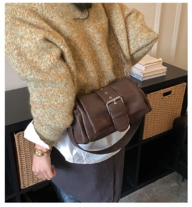 Detail of coffee brown leather shoulder bag with wide buckled strap in a home setting