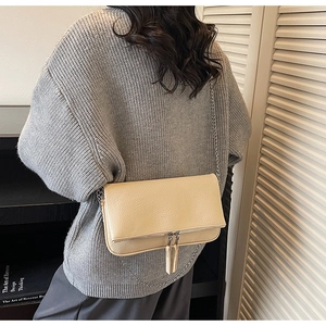 Detail shot of a beige lychee pattern envelope bag with silver chain and long tassels