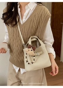 Close-up of beige leather bucket bag with pebble texture and cute plush bear charm