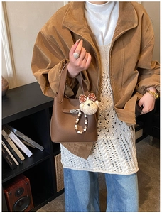 Détail d'un sac seau marron à motif litchi avec pendentif ours et fermoir en métal