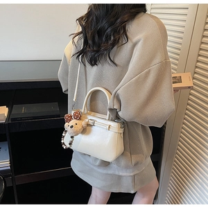 Sac à main beige avec boucle décorative et breloque ours porté par un mannequin