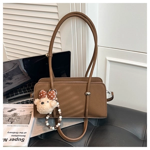 Detailed view of brown leather shoulder bag with a cute teddy bear charm and bow decoration