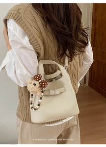 Close-up of minimalist beige bucket bag featuring lychee grain leather and cute bear charm