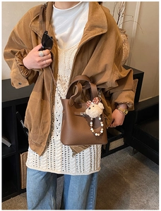 Détail d'un sac à main marron en cuir grainé avec une poignée et un pendentif en peluche