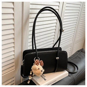 Detail of black lychee grain leather baguette bag with a cute teddy bear charm