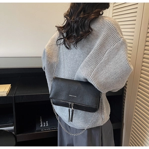 Detail of black pebble leather crossbody bag with silver chain strap and tassel zippers