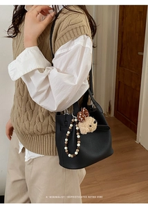 Detail of black pebbled leather bucket bag with cute plush puppy and beaded charms
